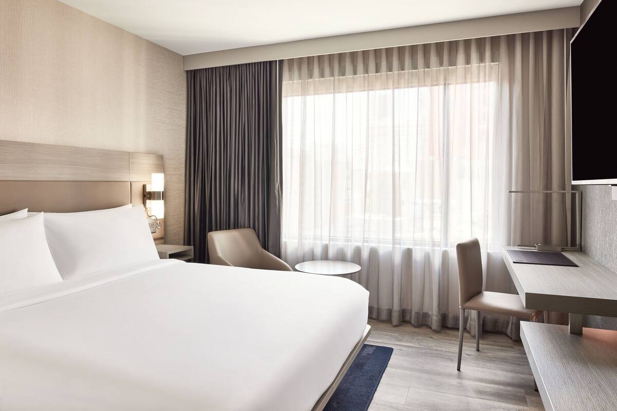 Ein Hotelzimmer mit einem großen Bett, einem Schreibtisch, einem Sessel und einem Fernseher.