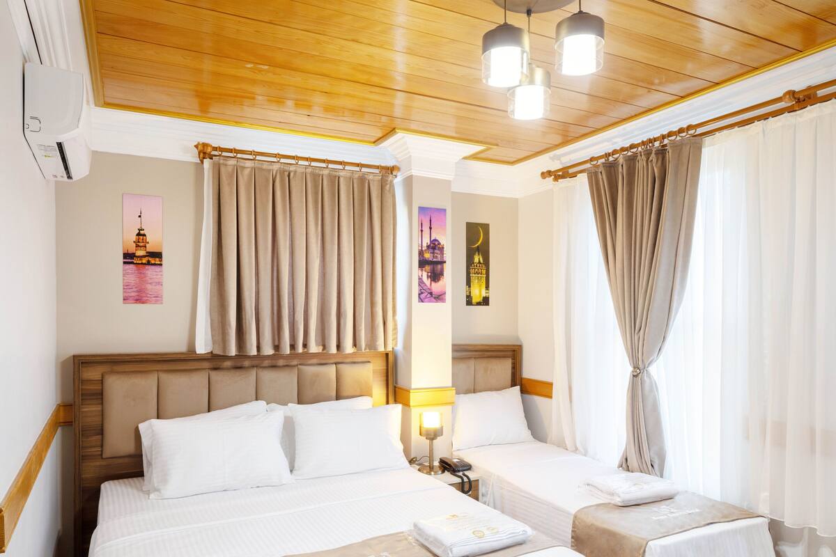 A hotel room with two beds, wooden flooring, a ceiling fan, and a nightstand with a lamp.