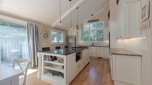 A modern kitchen with white cabinetry, a central island, pendant lighting, and a view of the outdoors through large windows.
