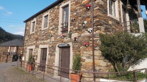 A stone building with a sign reading "CASA DO ADRO". It has multiple windows and doors, and potted plants are placed on the exterior walls. - Casa do Adro-Passadiços do Paiva (Espiunca)