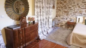 A bedroom with a stone wall, a wooden dresser, a bed with a white bedspread, and a large mirror on the wall. - Casa do Adro-Passadiços do Paiva (Espiunca)