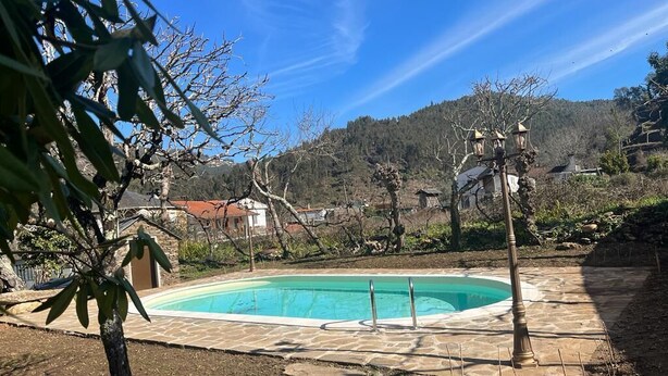 A swimming pool with a stone deck, surrounded by trees and a hilly landscape. - Casa do Adro-Passadiços do Paiva (Espiunca)