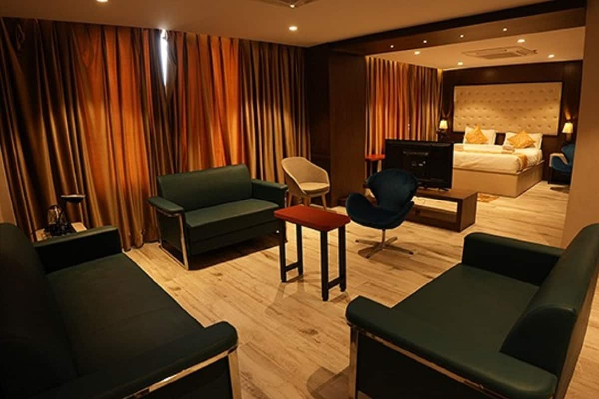 A hotel room with a green sofa, a red table, a blue chair, and a bed with a headboard.