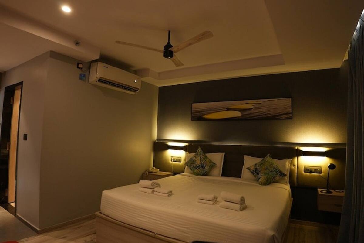 A hotel room with a bed, a ceiling fan, an air conditioning unit, and two bedside lamps.