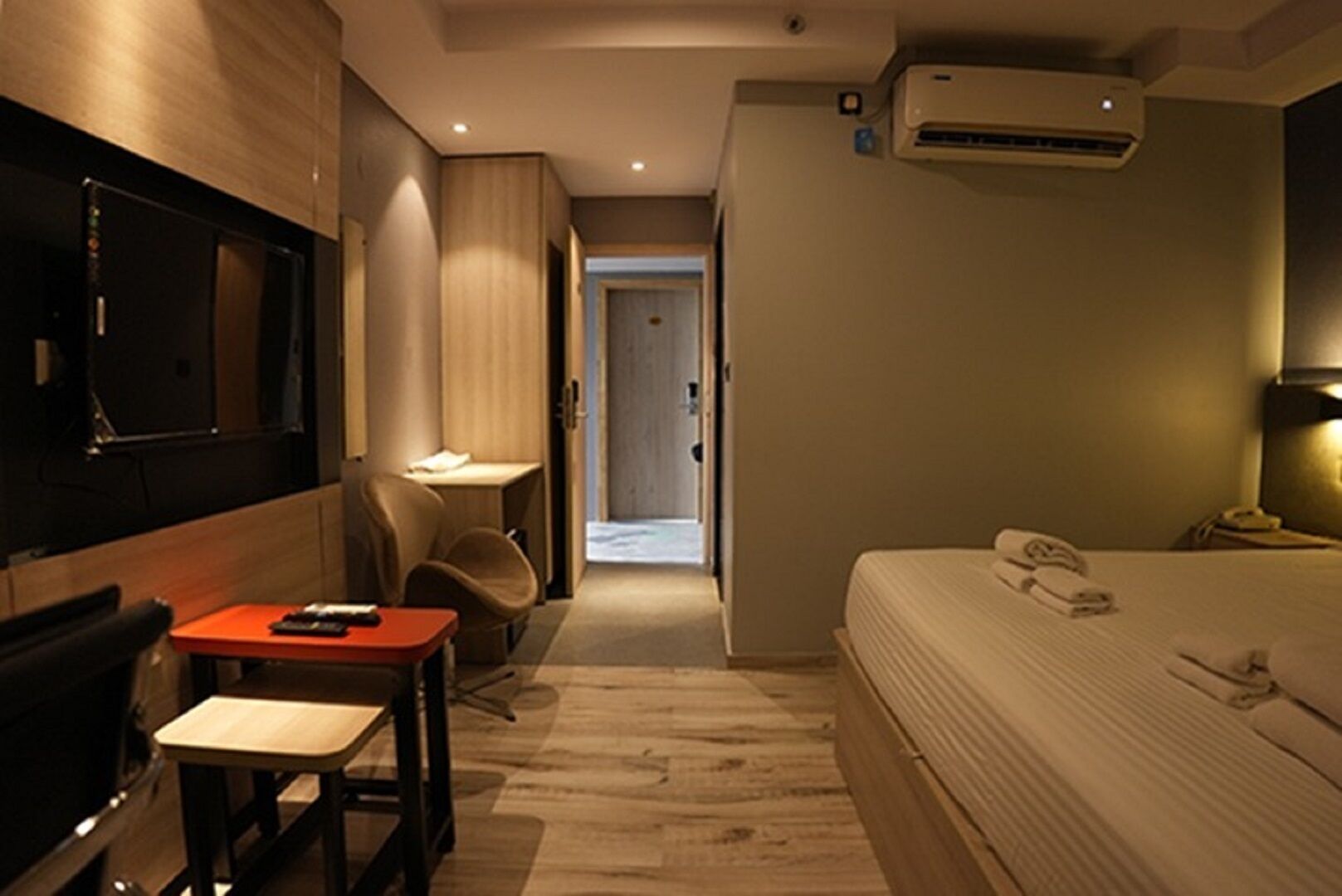 Habitación de hotel con cama, escritorio, silla, televisión y unidad de aire acondicionado.