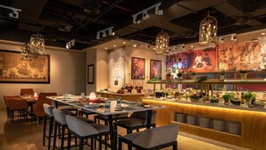 A restaurant with a bar area, tables, chairs, and a counter with food displays. - Four Points by Sheraton Production City, Dubai (Dubai)