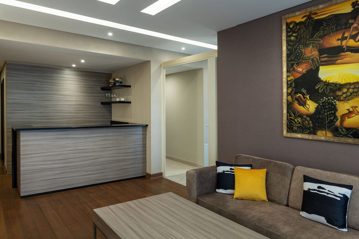 A modern living room with a sofa, a coffee table, and a kitchen area with a countertop and shelves.