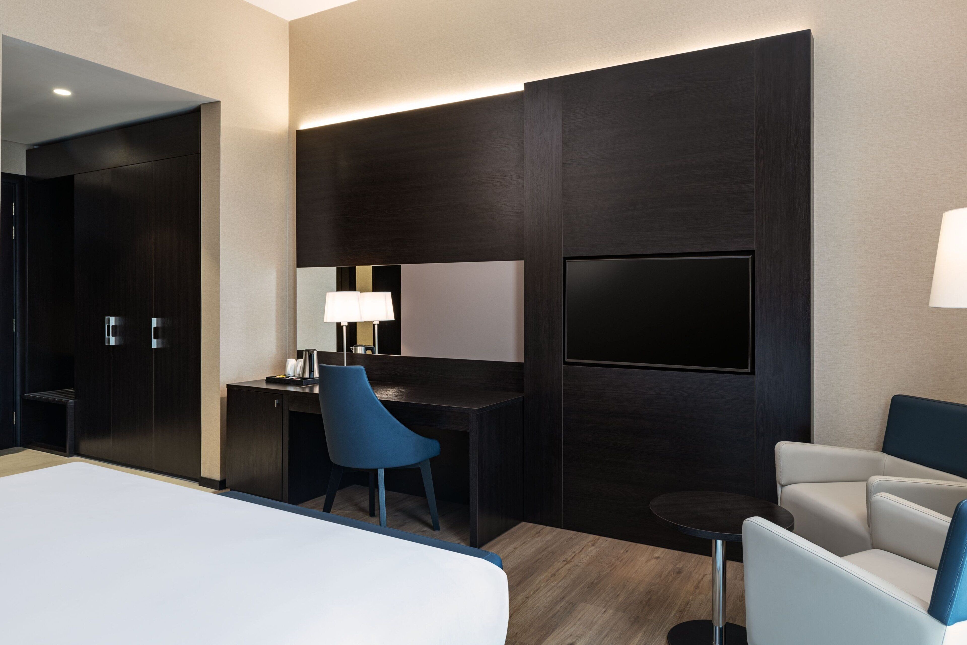 A hotel room with a large bed, a desk with a chair, a TV, and a small table.