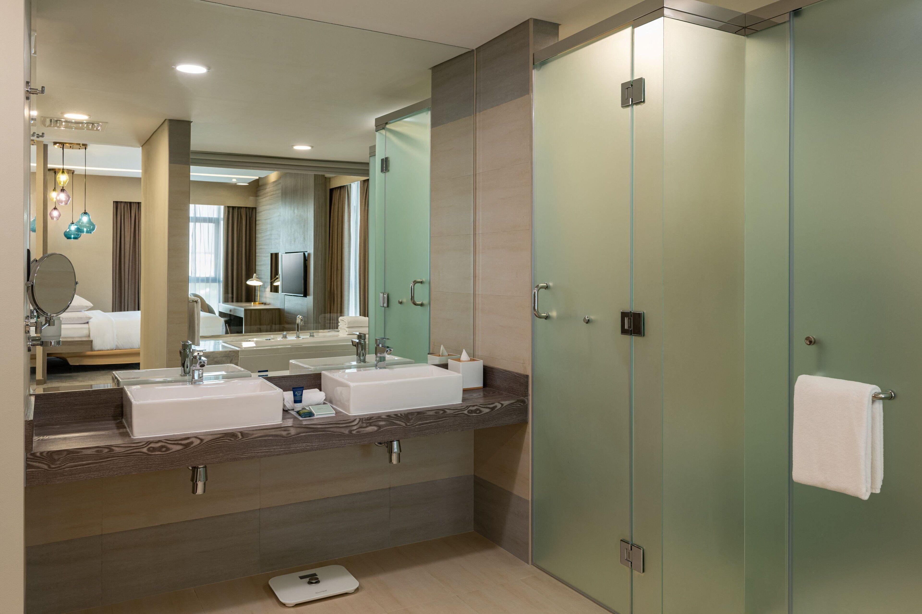 A modern bathroom with two sinks, a large mirror, and a glass shower enclosure.