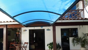 A covered outdoor area with a table and chairs, a potted plant, and a door leading inside. - Recanto das Tartarugas Aluguel Economico (Arraial do Cabo)