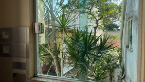 A window with a view of a garden, including various plants and a building in the background. - Recanto das Tartarugas Aluguel Economico (Arraial do Cabo)