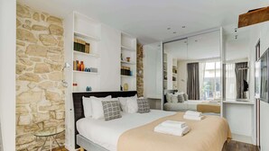 Une chambre moderne avec un mur en pierre, un lit avec une literie blanche, une table de chevet et une bibliothèque intégrée.
