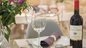 Une table à manger avec une bouteille de vin, un verre, du fromage et un vase rempli de fleurs.