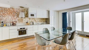 Une cuisine moderne avec des meubles blancs, un mur d’accent en pierre et une table à manger en verre, accompagnée de chaises.