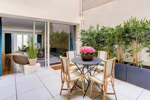 Une terrasse extérieure moderne, dotée d’une table ronde, de chaises en osier et de plantes en pot.