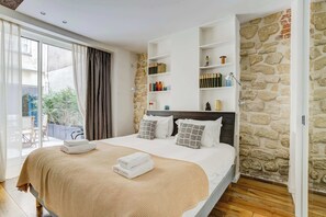 Une chambre avec un grand lit, un mur en pierre, une bibliothèque et une porte-fenêtre coulissante donnant sur un espace extérieur.
