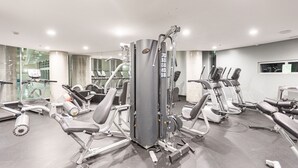 Une salle de sport équipée de divers appareils d’exercice, notamment des tapis de course et des appareils de musculation, et aménagée dans un espace vaste et lumineux grâce à de grandes fenêtres.