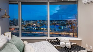 Une chambre avec une grande fenêtre donnant sur une vue panoramique de la ville la nuit.