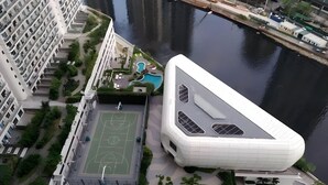 Un bâtiment moderne doté d’un toit incurvé original, d’un terrain de basketball et d’une piscine.