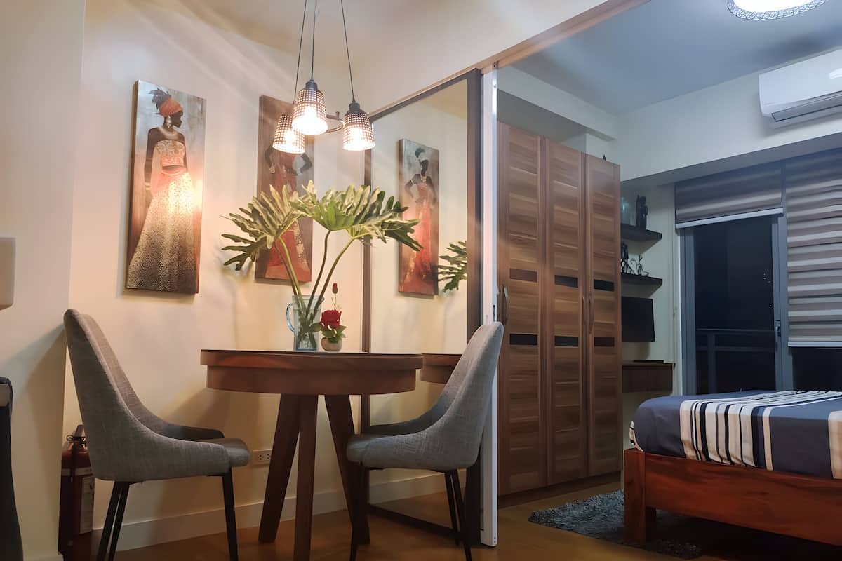 A modern bedroom with a wooden bed, a dining table with two chairs, and a large mirror.