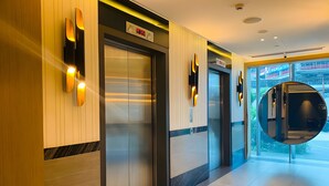 Un hall d’hôtel moderne doté d’ascenseurs, d’une horloge numérique et d’un grand miroir qui reflète l’intérieur.