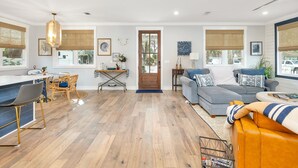 Un ampio soggiorno con pavimento in legno, un'area pranzo con tavolo e sedie, e un divano grigio con una coperta a righe.