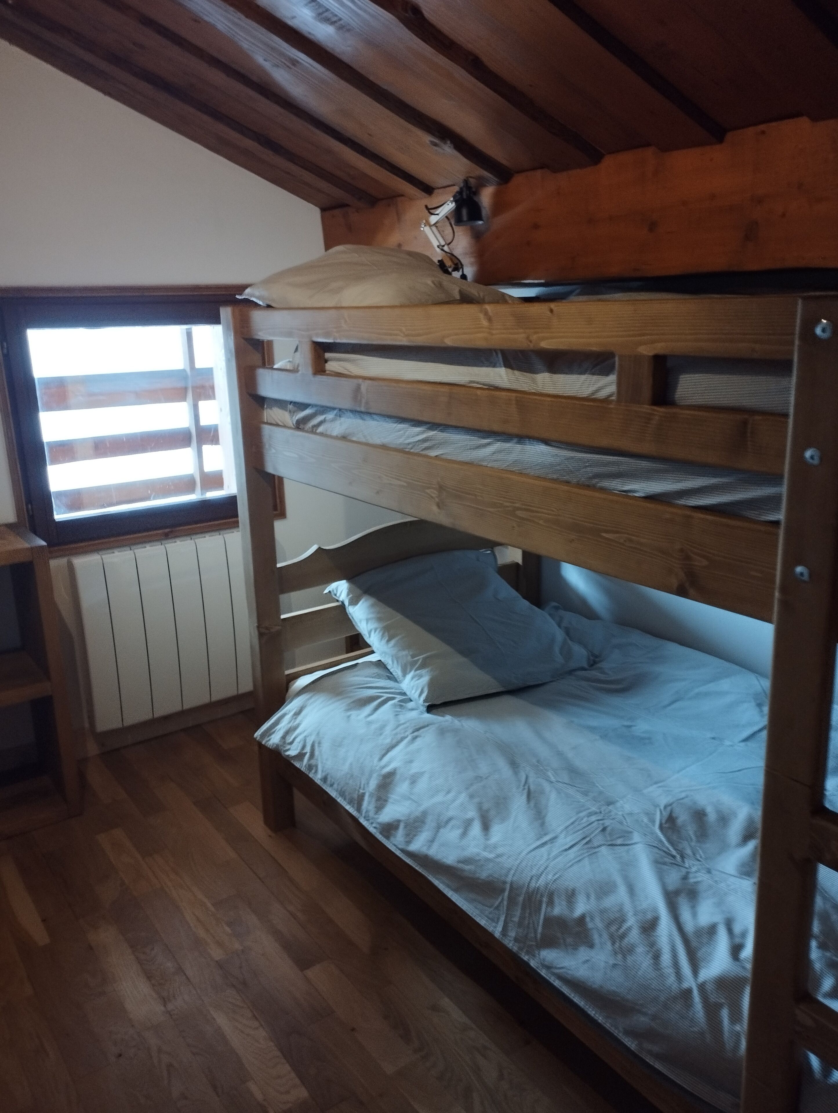 A bunk bed with a wooden headboard and a window with blinds.