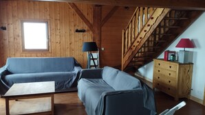 A cozy cabin interior with a wooden staircase, a blue sofa, a small table, and a dresser with heart-shaped drawers.
