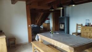 A spacious room with a large wooden table, benches, a fireplace, and a staircase leading to an upper level.