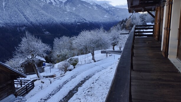 A wooden balcony overlooking a snow-covered landscape with mountains in the background.