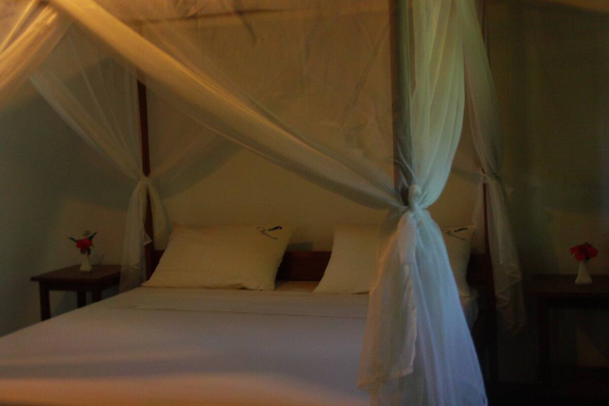A bed with a canopy, a nightstand with a vase, and a wall-mounted clock.
