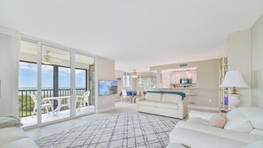 A spacious living room with a large sofa, a patterned rug, and a balcony with a view of the ocean. - 8th Floor Oceanview! Large Balcony ~ Steps to Vanderbilt Beach (Naples)