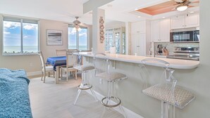 A modern kitchen with a bar area, large windows, and a view of the ocean. - 8th Floor Oceanview! Large Balcony ~ Steps to Vanderbilt Beach (Naples)