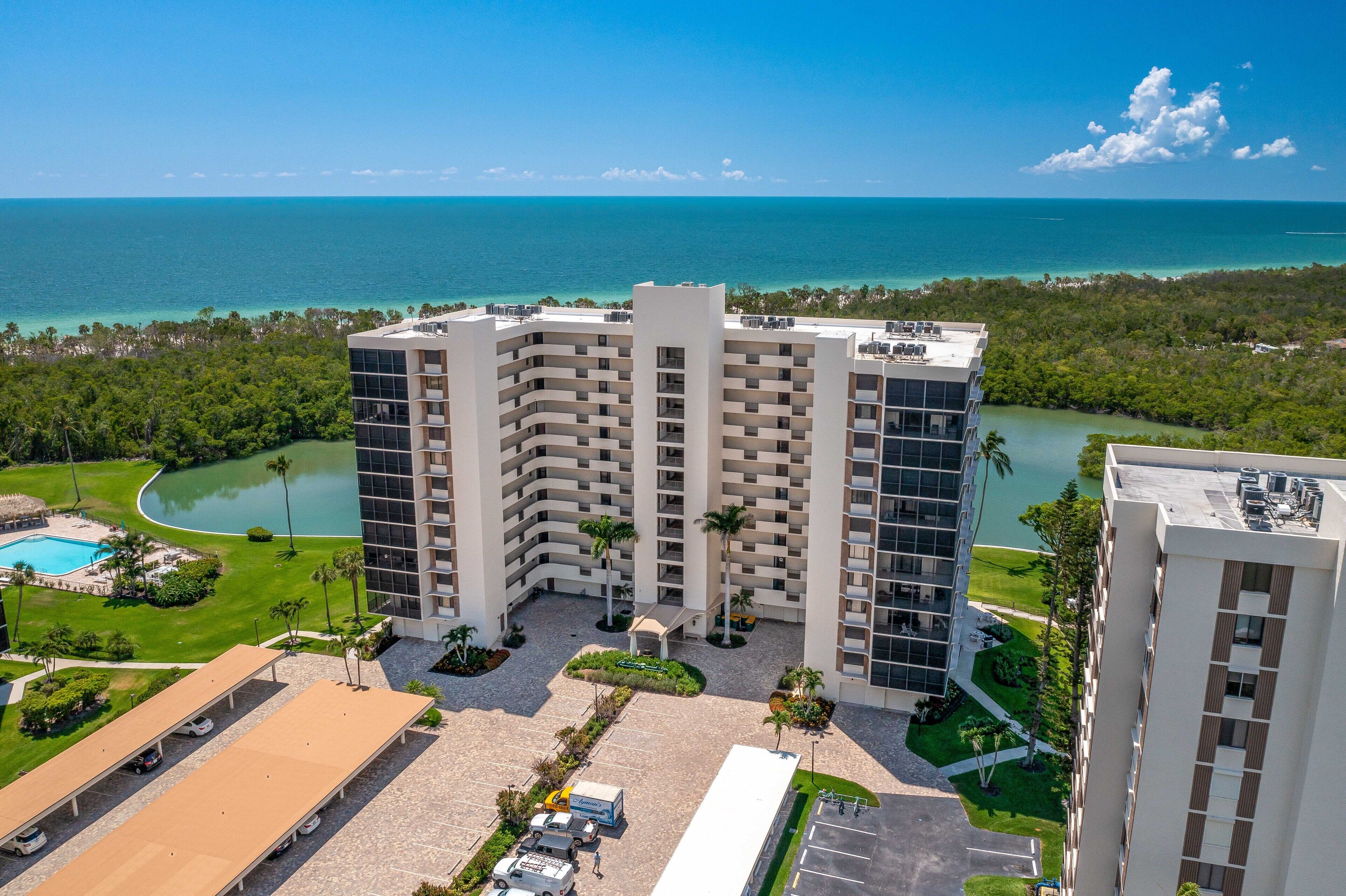 A high-rise hotel with a pool, surrounded by greenery and a view of the ocean.