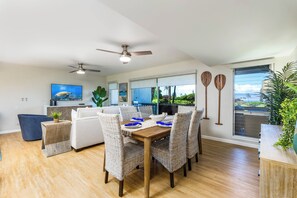 A modern dining area with a wooden table, wicker chairs, and a ceiling fan.