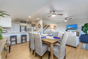 A modern kitchen with a stainless steel refrigerator, a dining area with wicker chairs, and a living room with a sofa and a television. - 3BR Ka’anapali Retreat | Ocean Views, Gorgeous renovation, Walk to Beach (Lahaina)