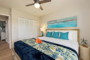 A bedroom with a bed, a ceiling fan, a painting, and a nightstand.