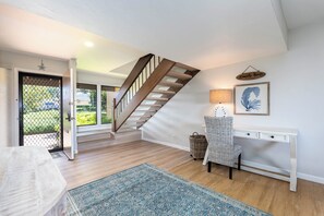 A staircase leading to a second floor, a desk with a lamp, a wicker basket, and a patterned rug.