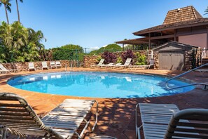 A swimming pool with lounge chairs, a stone wall, and a building with a tiled roof.