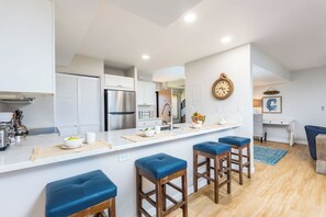 A modern kitchen with white cabinetry, a stainless steel refrigerator, and a central island with stools.