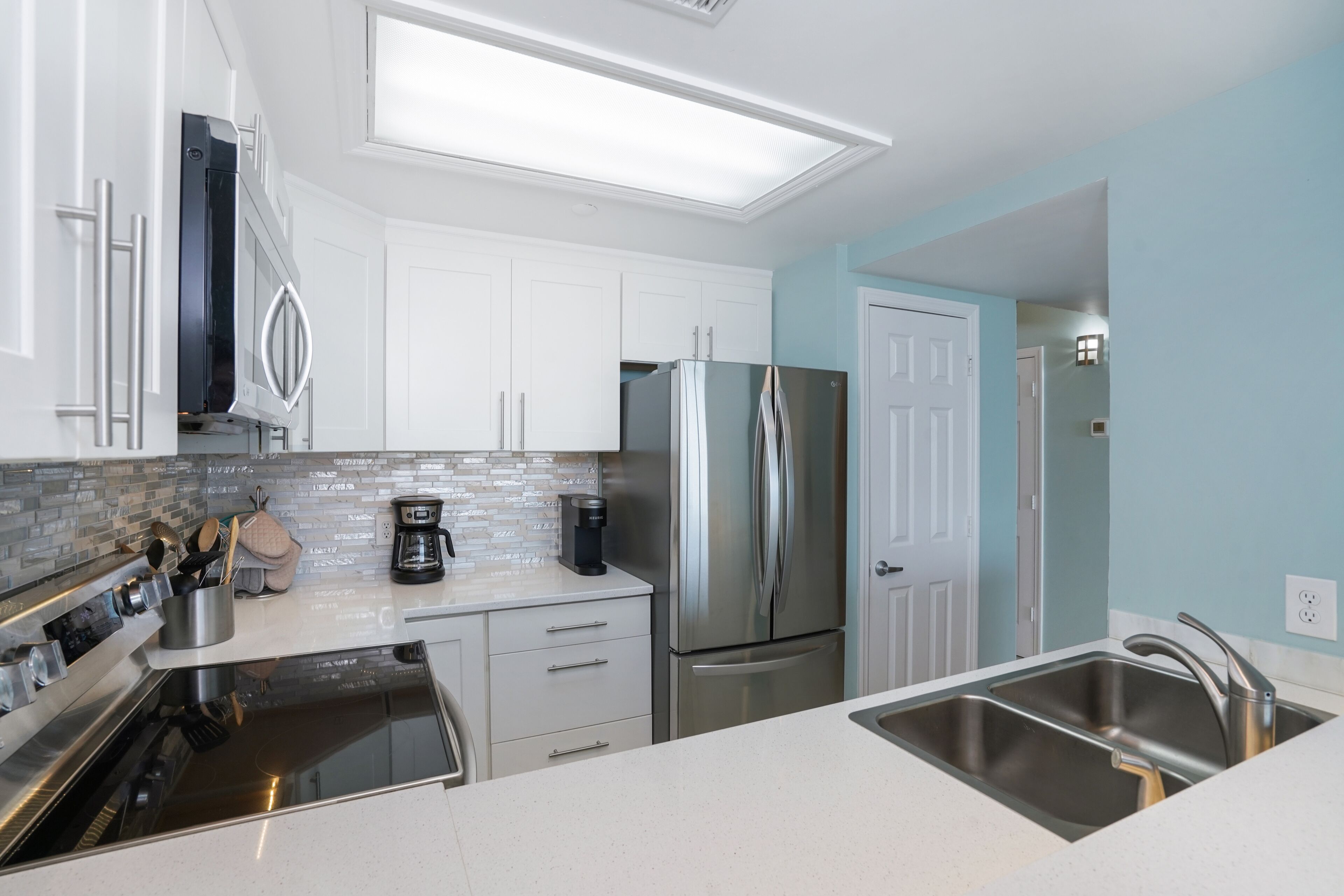 Una cocina moderna con armarios blancos, electrodomésticos de acero inoxidable, un lavamanos doble y salpicadero de azulejos.
