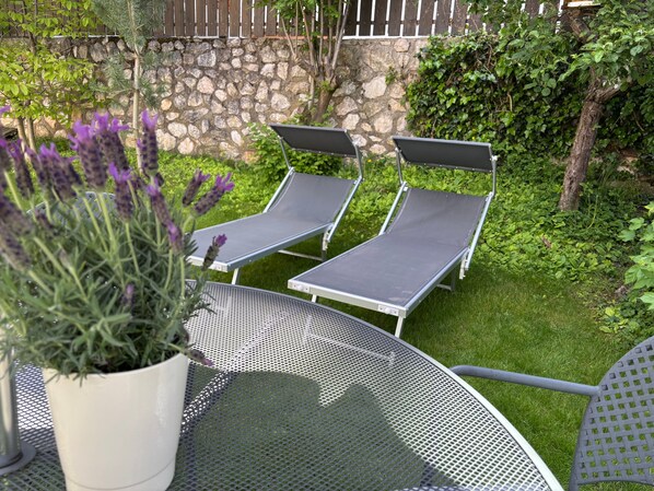 Un patio con dos sillones de descanso, una mesa de metal y una maceta con flores moradas.