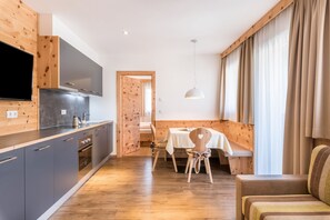 Eine moderne Küche mit grauen Schränken, einem eingebauten Ofen und einem Flachbildfernseher. Ein Essbereich mit Tisch und Stühlen sowie eine Couch mit gestreifter Sitzkissen sind ebenfalls vorhanden.