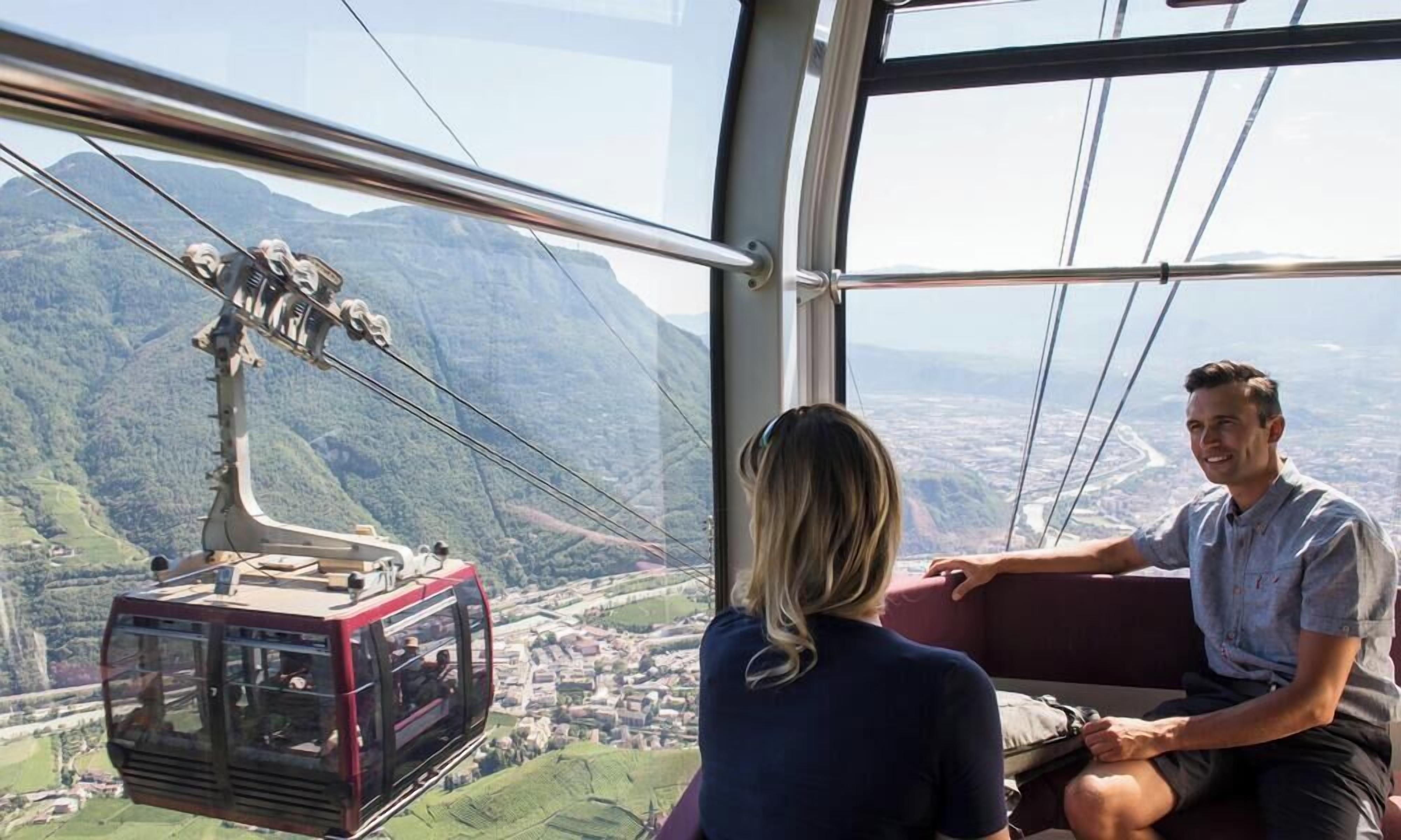 Eine Standseilbahn mit Fahrgästen, einer Stadtlandschaft und Bergen im Hintergrund.