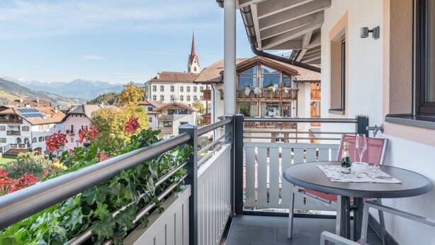 A balcony with a table, a chair, and a glass of champagne. - Apartments Marialisa Superior 'Apt Tulpe' with Mountain View, Whirlpool & Wi-Fi (Chiusa)