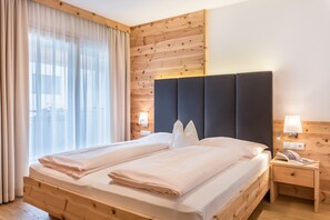 A double bed with a wooden headboard, a nightstand with a lamp, and a window with curtains.