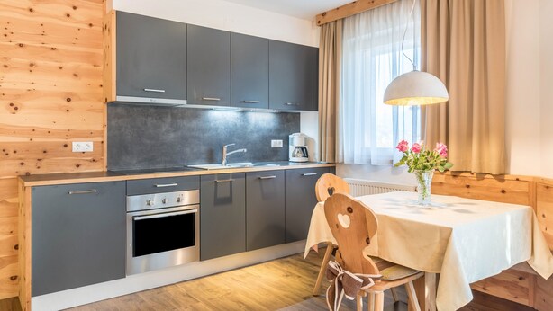A modern kitchen with grey cabinets, a wooden dining table, and a pendant light.