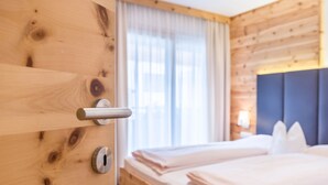 A wooden room with a bed, a window with curtains, and a door with a handle. - Apartments Marialisa Superior 'Apt Rose' with Mountain View, Whirlpool & Wi-Fi (Chiusa)