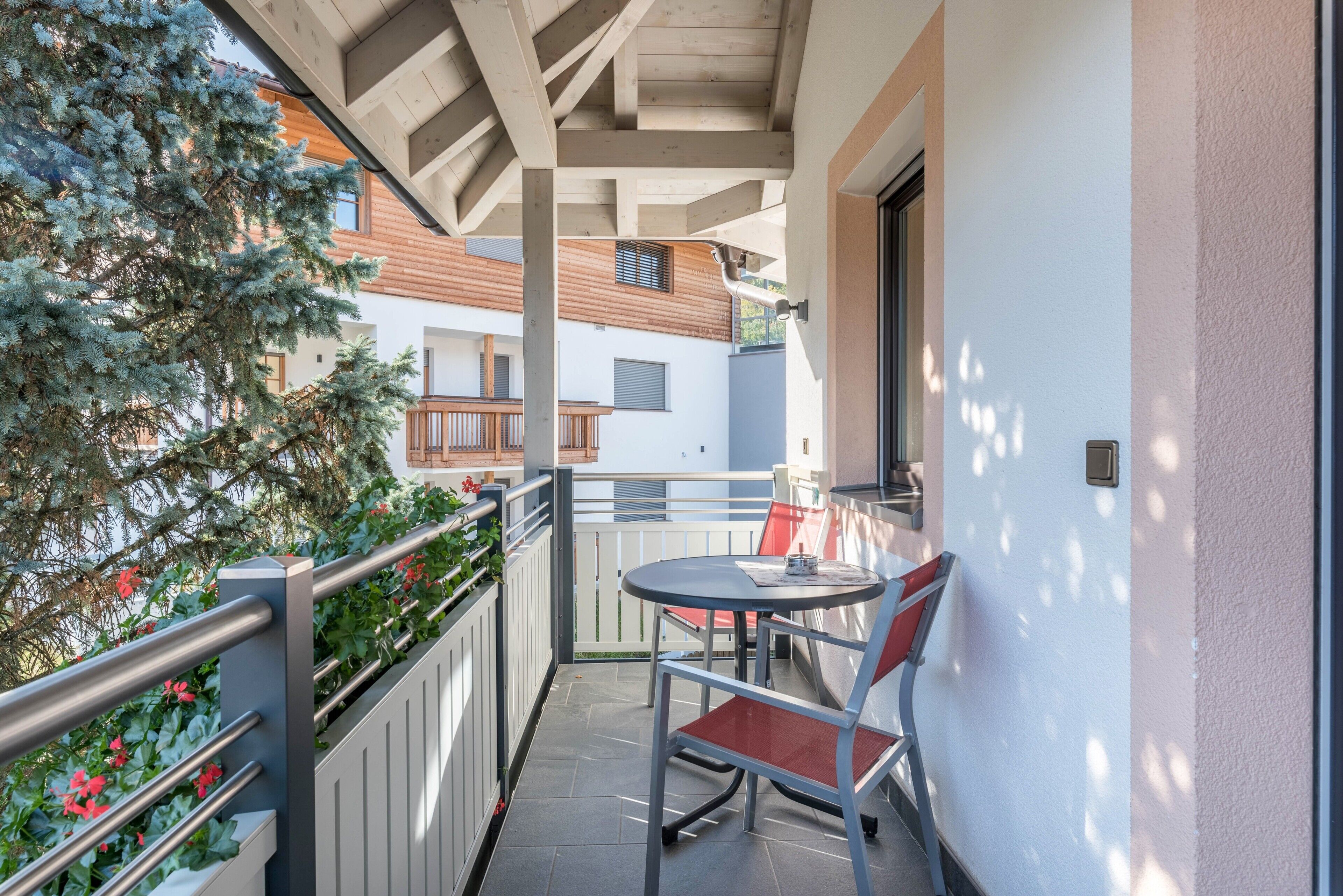 Varanda com mesa e cadeira, corrimão e vista para edifícios próximos.