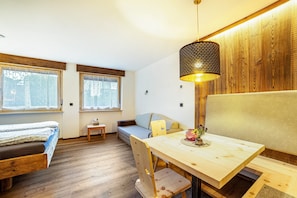 Une pièce avec un plancher en bois, un lit, un canapé, une table à manger avec des chaises et un luminaire suspendu.